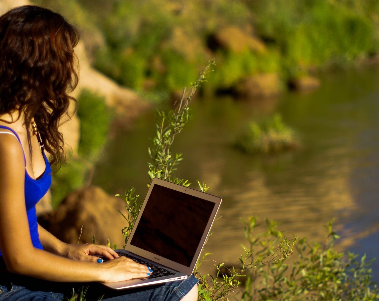 Kobieta w niebieskiej bluzce pracuje na laptopie na łonie natury