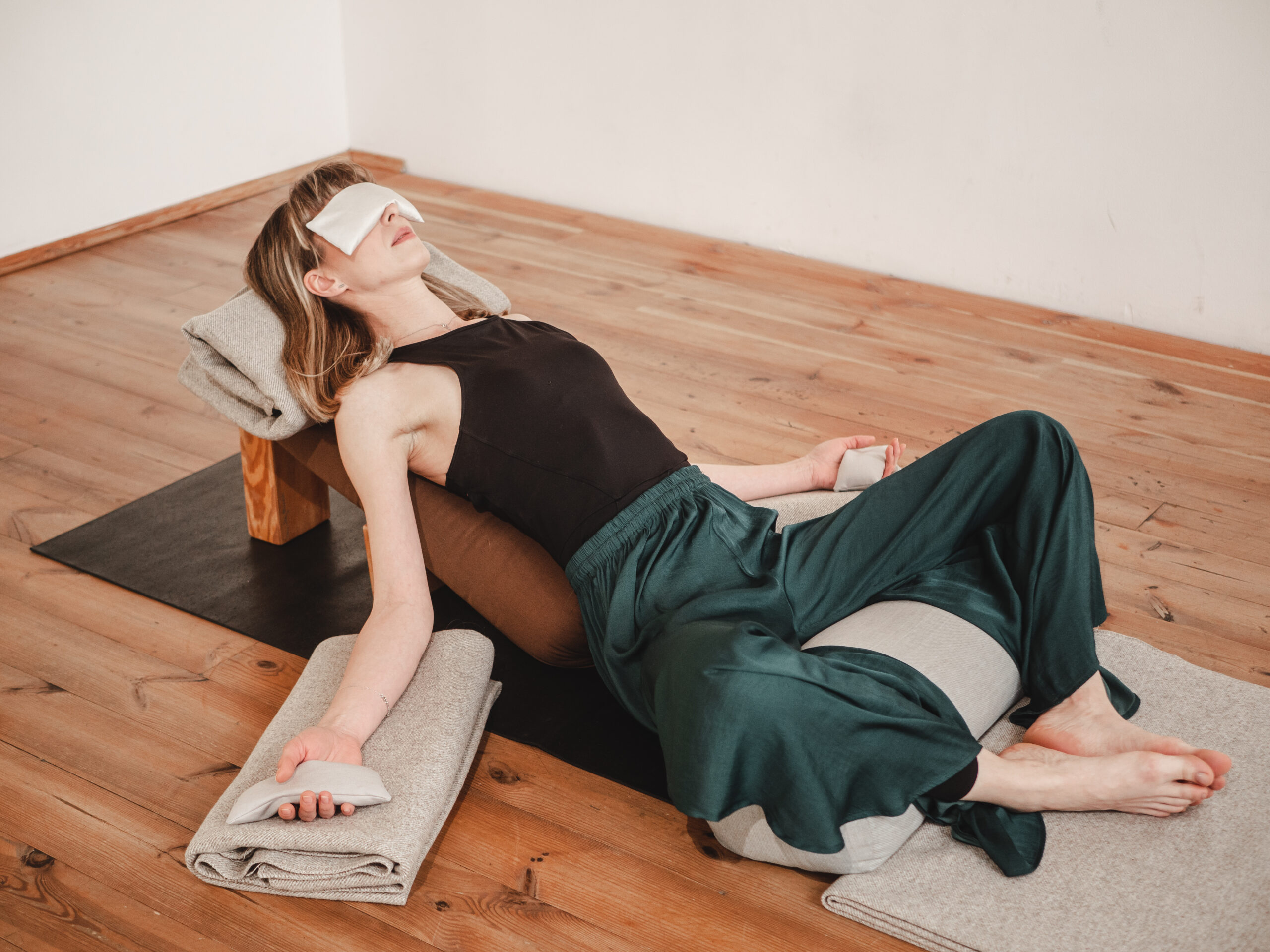 KObieta w czarnej koszylce i zielonych spodnaich ćwiczy jogę restorative