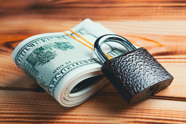 Plik banknotów złączony gumką i zamknięta kłódka leżą na drewnianym stole