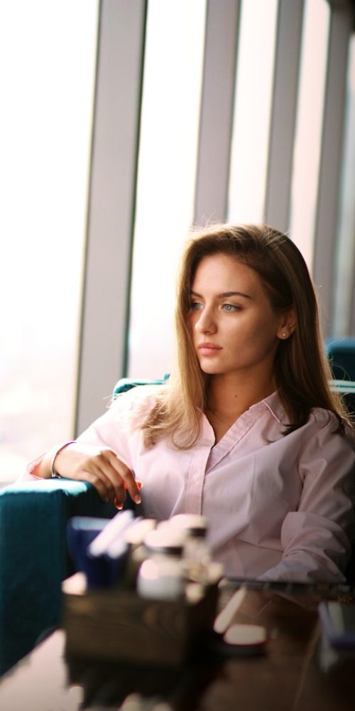 Kobieta w białej bluzce siedzi zamyślona w fotelu